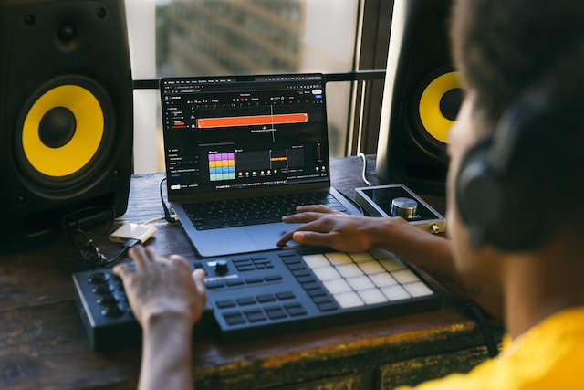 man in yellow shirt on headphones creating music on his midi controller and laptop